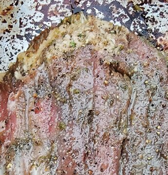 close up of flank steak tip showing fat on edge, and marinade covering.