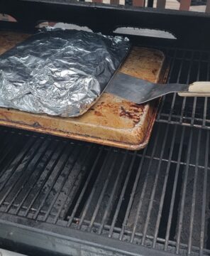 foil packet of potatoes, being slid from pan onto top rack of grill using offset spatula