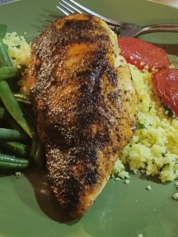 Plated blackened chicken breast with couscous, green beans, and roasted tomatoes