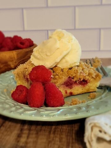 finished plated raspberry buckle with ice cream on top, garnished with fresh raspberries, bowl of raspberries shown in background