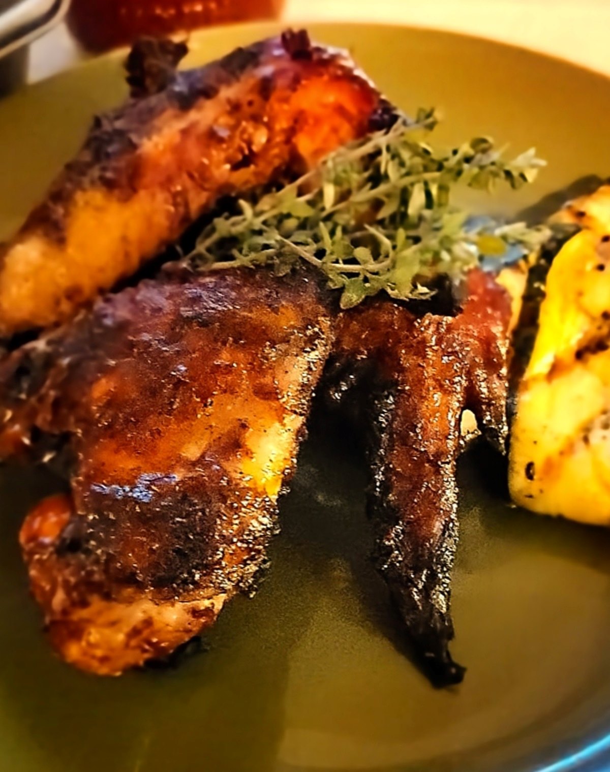 Plated barbecued chicken wings with fresh thyme garnish and grilled vegetables.