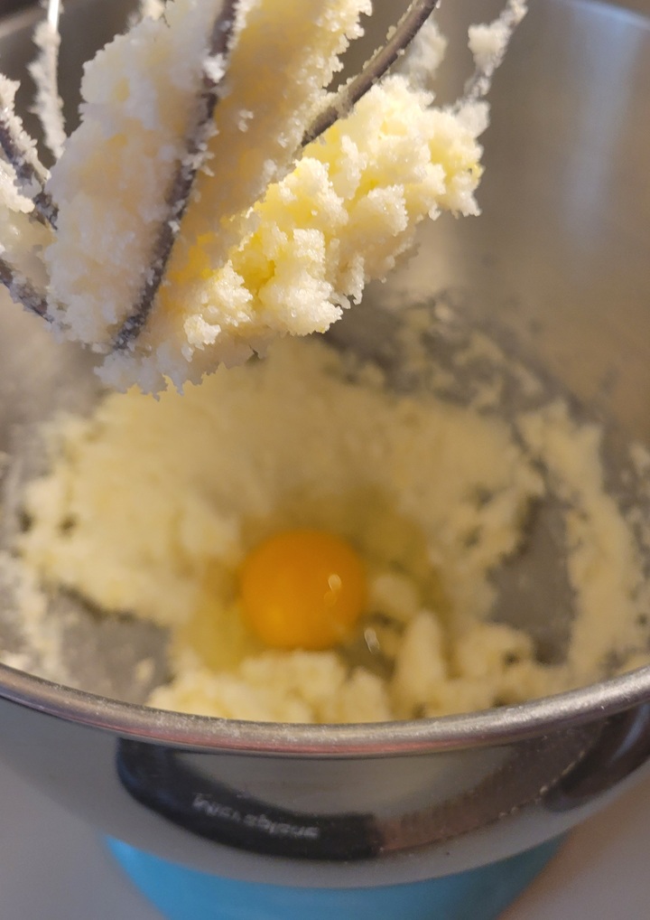 close up of mixer attachment showing yolks and sugar combined, background showing an additional egg yolk just added