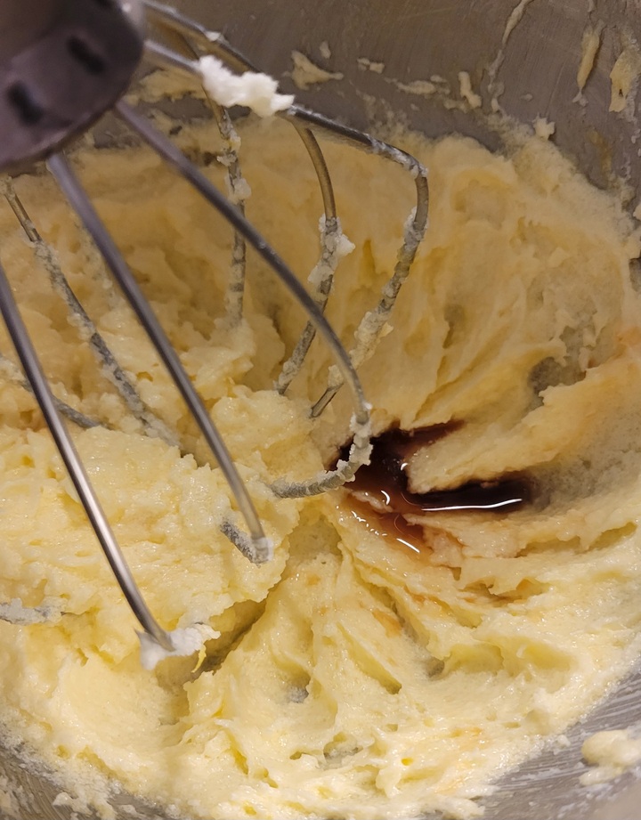 batter being beaten in mixer bowl, small pool of vanilla extract just added