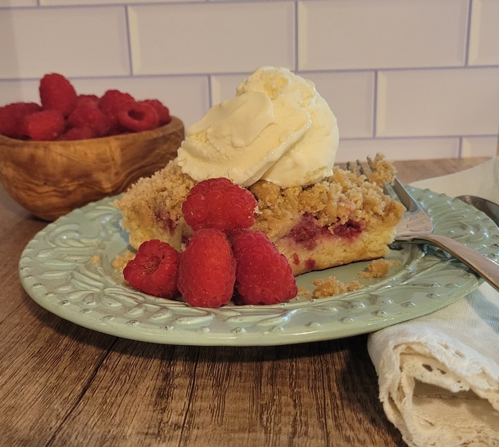 finished plated raspberry buckle with ice cream on top, garnished with fresh raspberries, bowl of raspberries shown in background