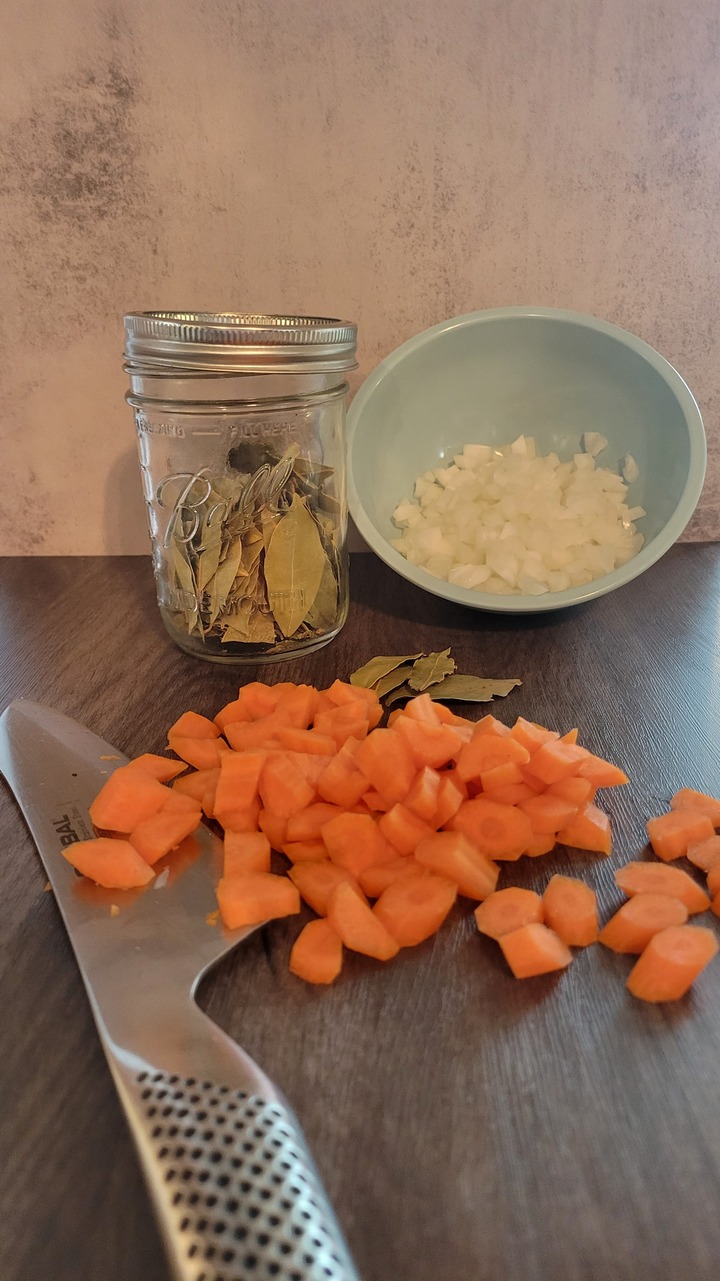 cutting board, knife, chopped carrot, onion, jar of bay leaves