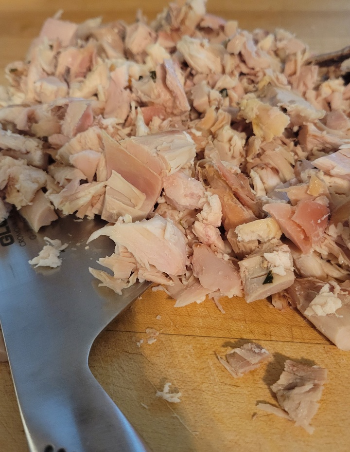 close up of chopped chicken for chicken salad on cutting board with knife