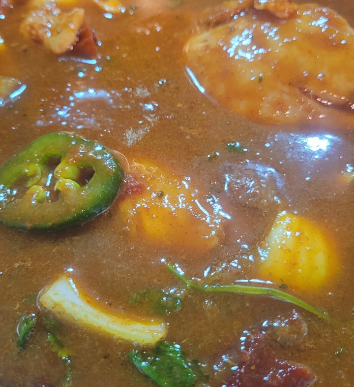 close up of chicken cooking in broth/sauce with jalapeno, cilantro and chunk of yellow onion showing through