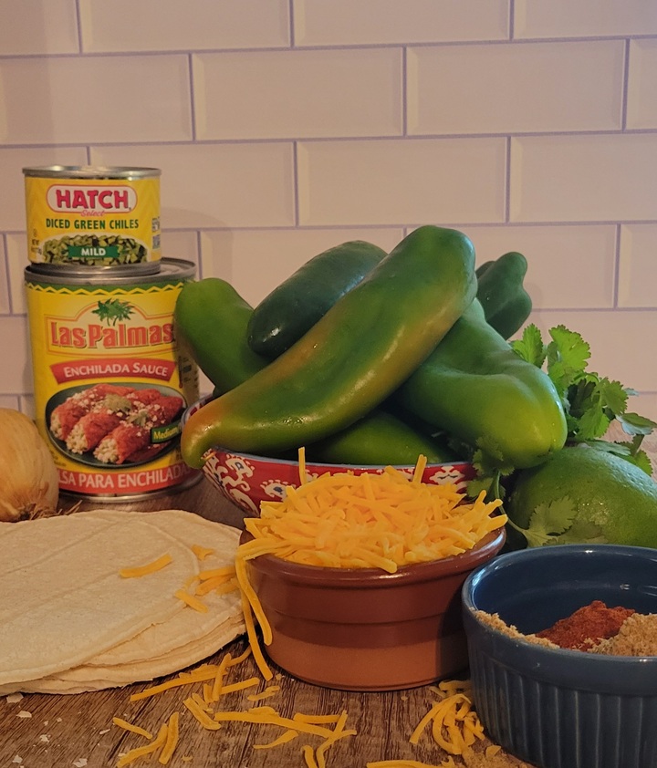 Ingredients for chicken enchilada casserole; yellow onion, canned green chilies, canned enchilada sauce, whole fresh green anaheim chilies, cilantro, lime, cry cumin and chili powder, shredded cheddar cheese, and fresh corn tortillas