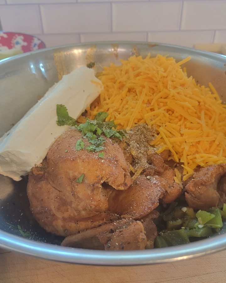 ingredients for chicken enchilada casserole filling; cream cheese, shredded cheddar, cooked chicken, dry seasonings, cilantro and roasted green chilies