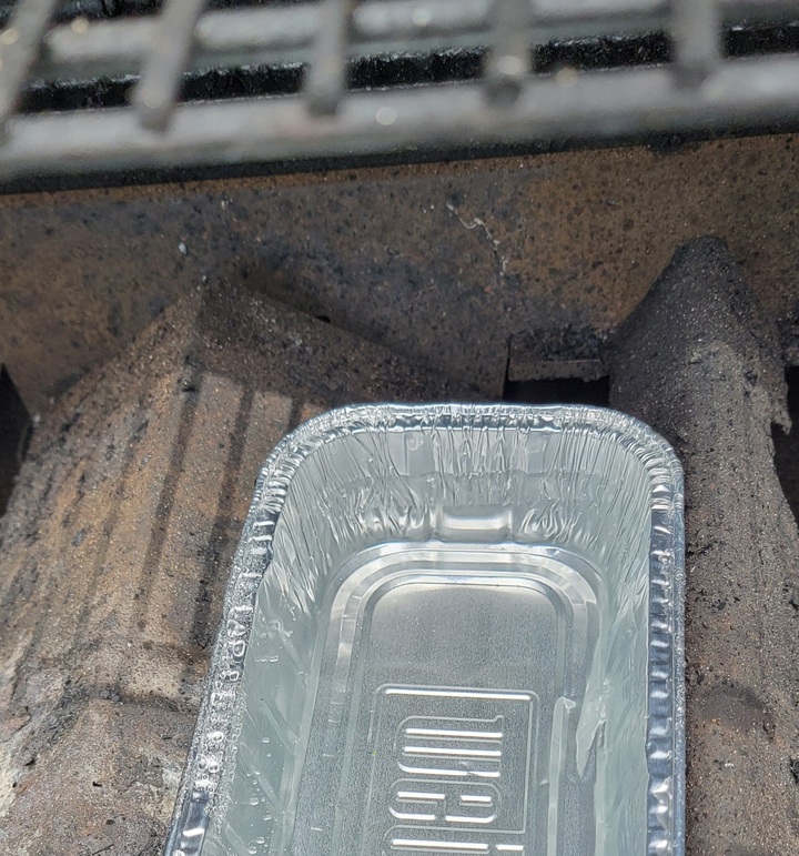 foil pan filled with water shown on fire baffles of grill, under grill grates