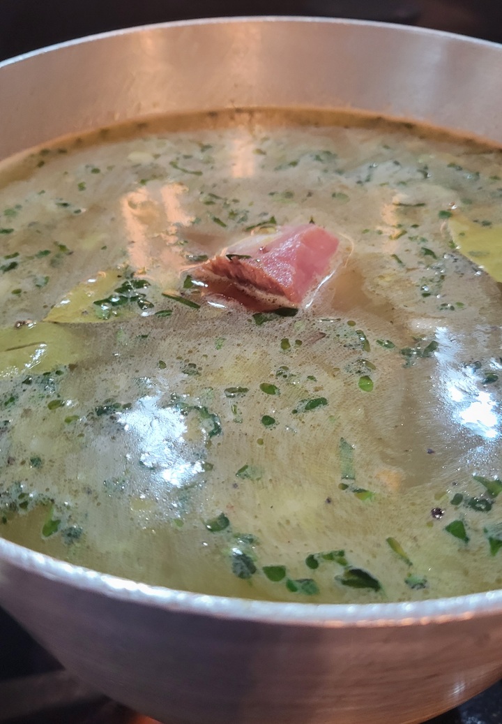 pot of broth with herbs and bay leaves floating, ham poking through the surface