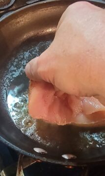 close up of chicken breast being placed in pan to blacken