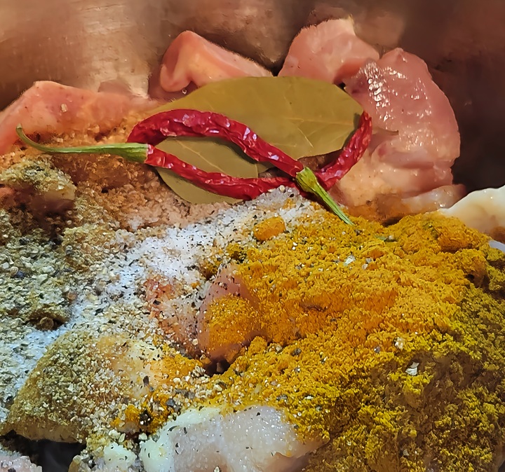 raw chicken, dry chilies, bay leaves, and dry spices, all shown together in bowl