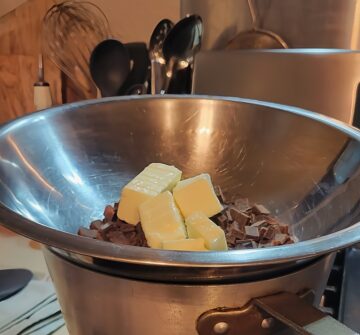 chopped chocolate and butter chunks shown in metal mixing bowl over sauce pan forming a double boiler