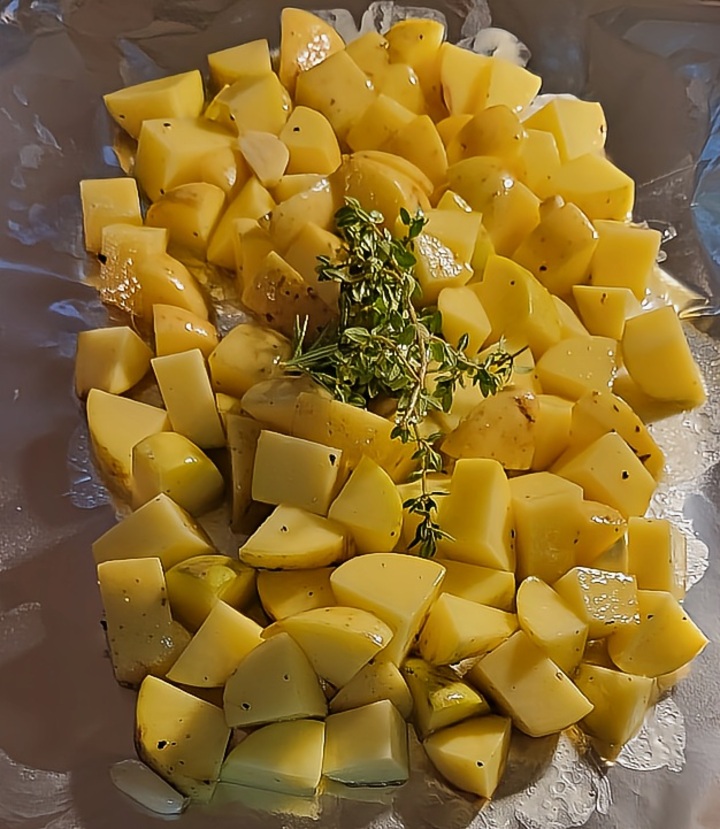 chopped and seasoned potatoes, topped with herb sprigs, on aluminum foil