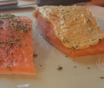two raw pieces of salmon, one sprinkled with herbs, the other shown with mustard on top