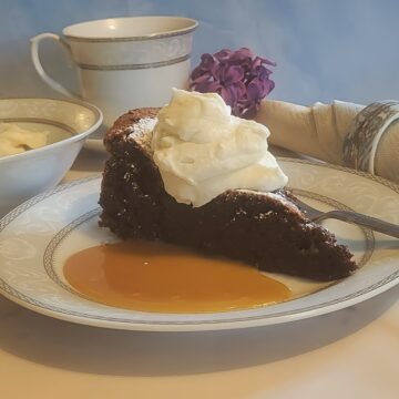 plated chocolate torte with caramel sauce, whipped cream. on decorative plate with flowers in background