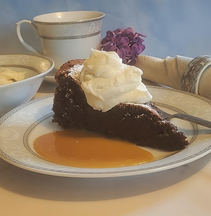 plated flourless chocolate torte with caramel sauce, whipped cream. on decorative plate with flowers in background
