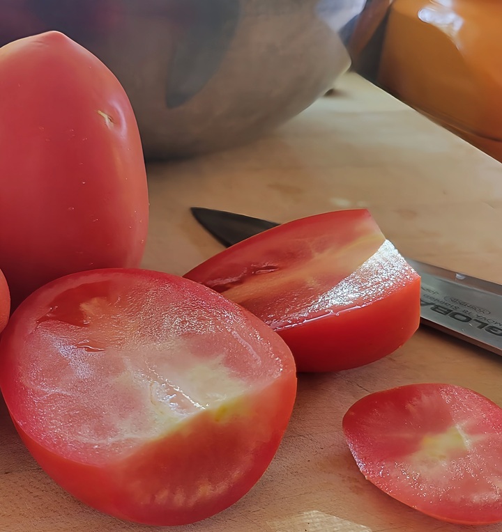 cutting board showing tomatoes, with tops cut off and halved