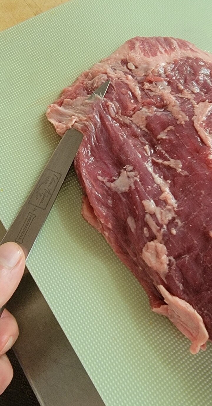 slim knife shown sliding under silver skin of flank steak