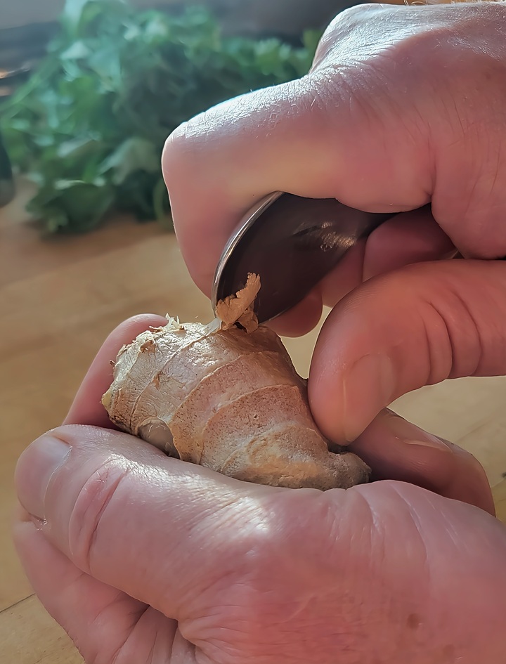 close up of raw ginger being peeled with the edge of a spoon