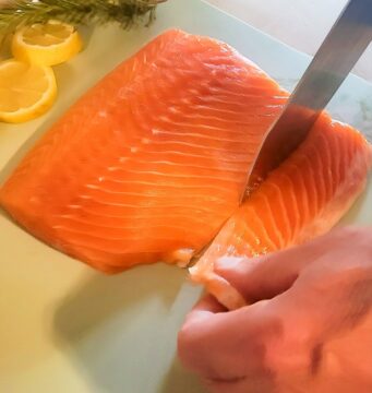 salmon belly being removed, hand holding it in place while knife cuts through