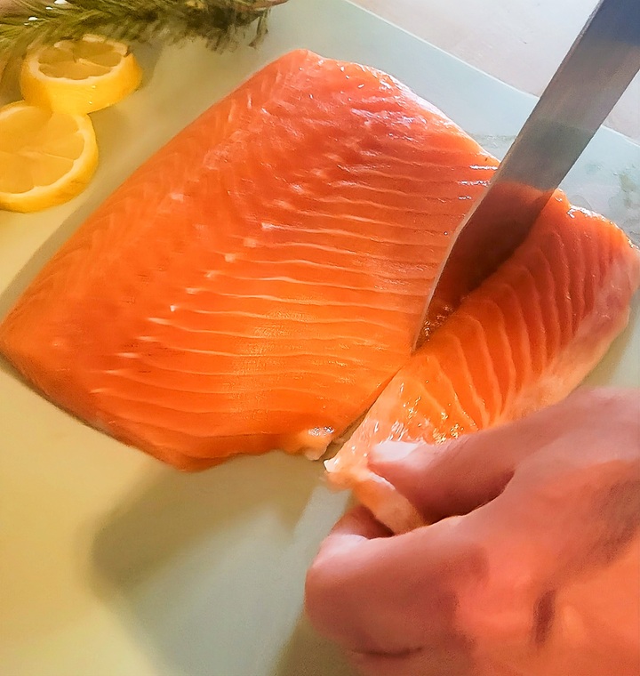 salmon belly being removed, hand holding it in place while knife cuts through