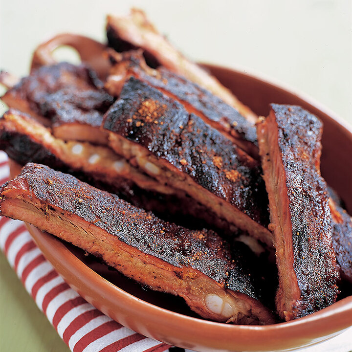 a serving dish filled with barbecued ribs with dry rub clinging to bark