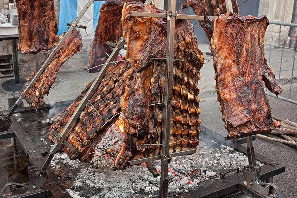 large pieces of meat held at an angle over hot coals to cook