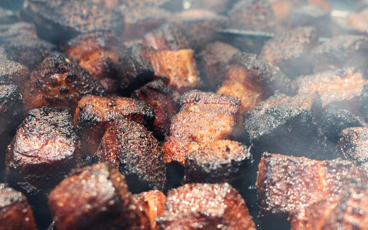 dark charred cubes of brisket shown cooking and smoking.