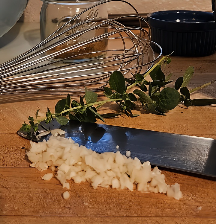 wooden cutting board with sprigs of fresh oregano, minced fresh garlic, knife.