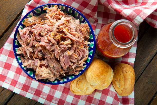 pulled barbecued pork meat in a serving bowl with a carafe of sauce, rolls.